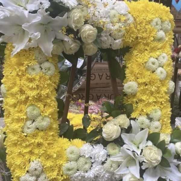 Yellow floral wreath with white lilies and roses on a stand
