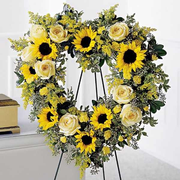 Heart-shaped floral wreath with sunflowers and cream roses on a stand