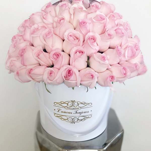 Round box of pale pink roses tightly arranged in a white hatbox with gold script label