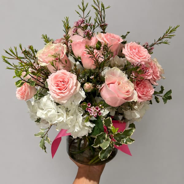 Pink roses and white hydrangeas in a glass vase with a pink ribbon