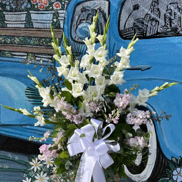 Tall white floral standing spray with a white ribbon on an easel