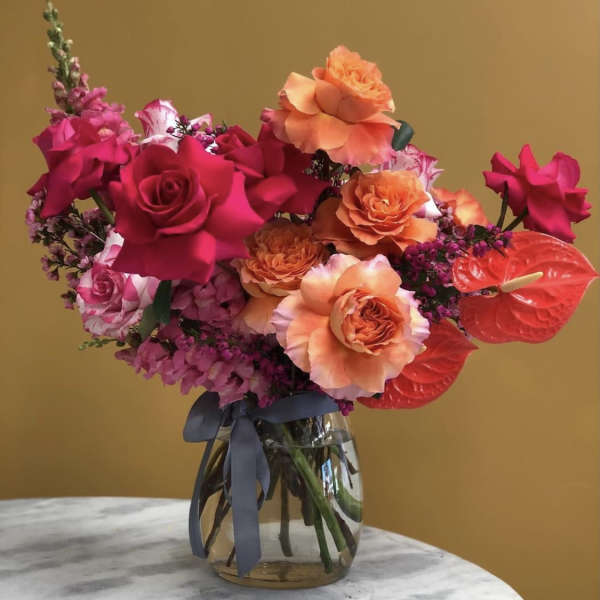 Bright pink and orange rose bouquet in a glass vase with a ribbon