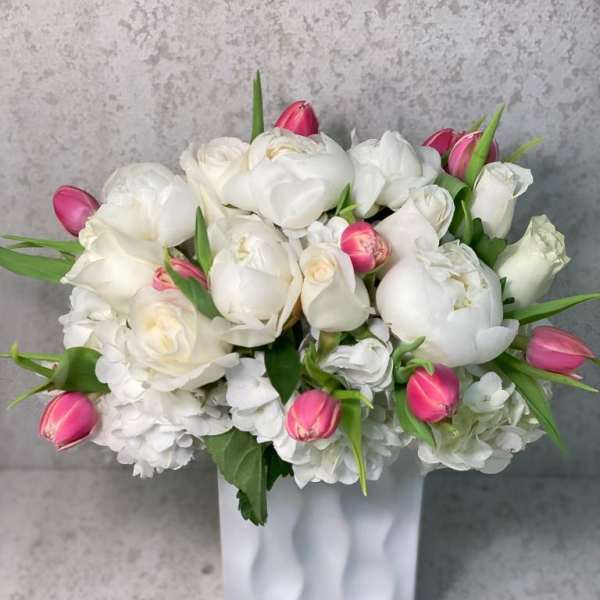 White tulips and roses arranged in a white vase with pink tulip buds