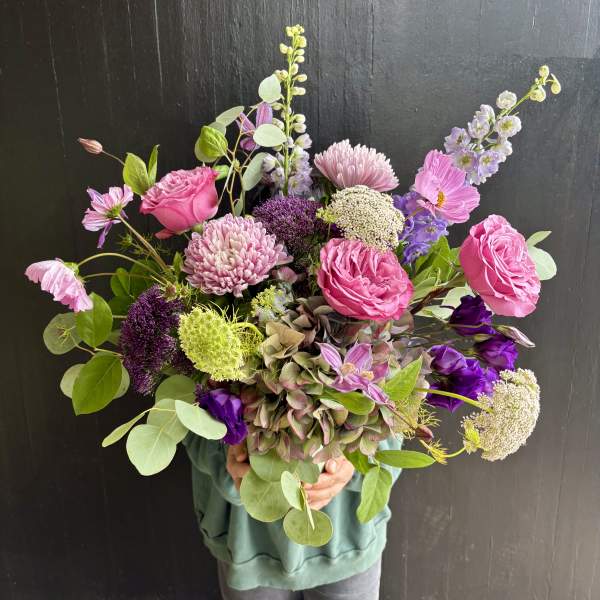 Handheld bouquet of pink and purple flowers with airy greenery