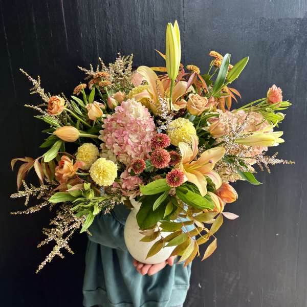 Mixed bouquet of peach and pink flowers in a white vase