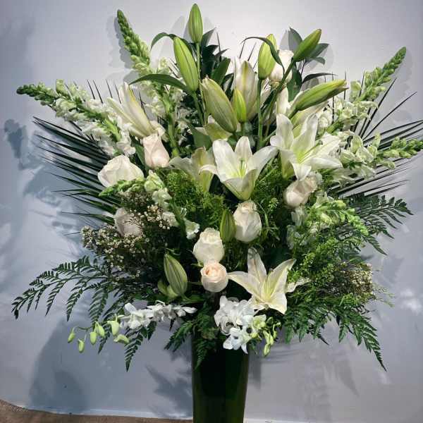 Tall white lily and rose arrangement in a dark glass vase