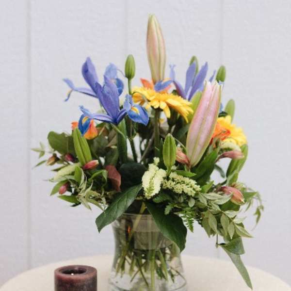 Mixed bouquet in a clear glass vase with a candle beside it