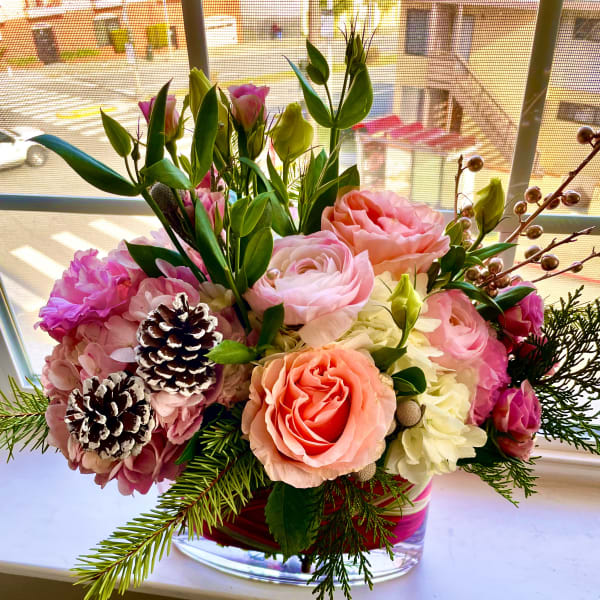Pink and peach floral arrangement in a clear glass vase with pinecones