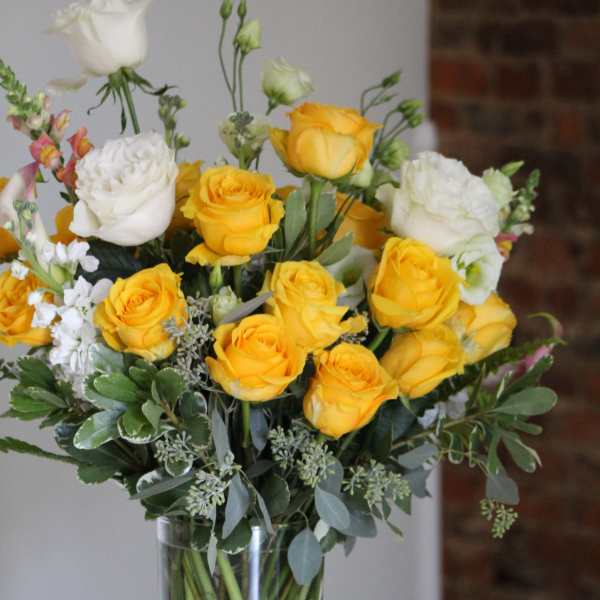 Yellow and white roses arranged in a clear glass vase.