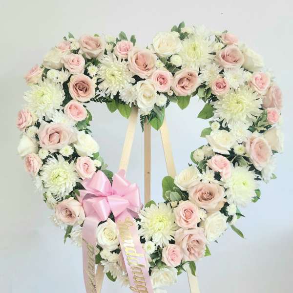 Heart-shaped floral wreath of pink and white roses on a wooden easel
