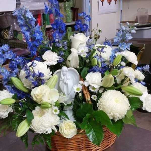 White and blue floral arrangement in a wicker basket with a small angel figurine