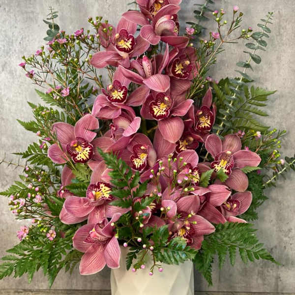 Pink orchid arrangement in a white vase with fern accents
