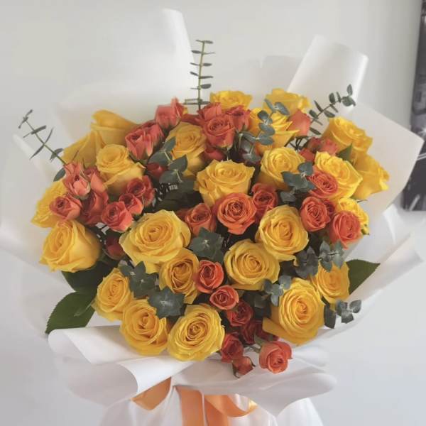Bouquet of yellow and coral roses wrapped in white paper with an orange ribbon