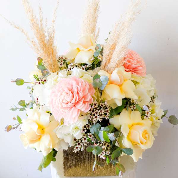 Pastel floral arrangement with roses and a pink dahlia in a gold vase