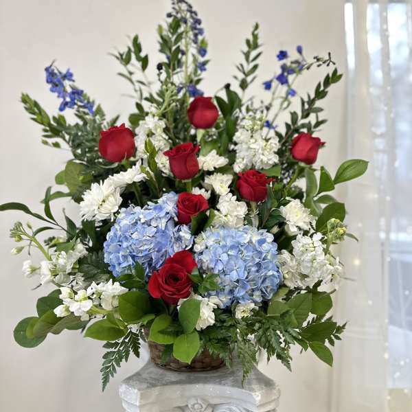 Red roses, blue hydrangeas, and white flowers in a basket arrangement