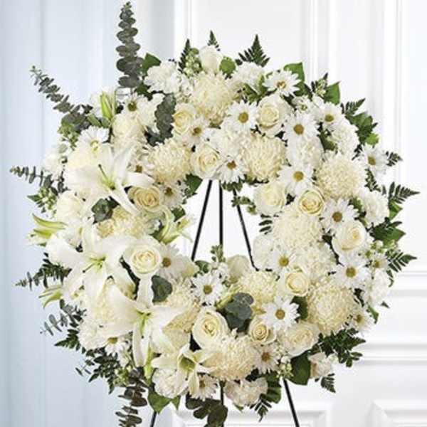 White floral wreath on a black easel with lilies, roses, and daisies