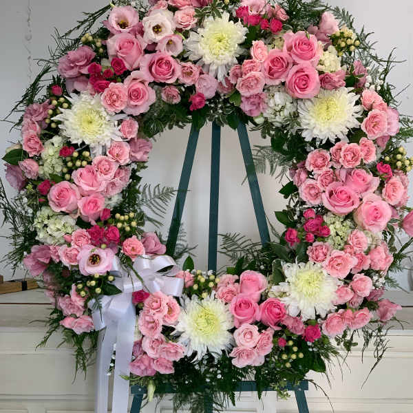 Large pink and white floral wreath on an easel with a white ribbon