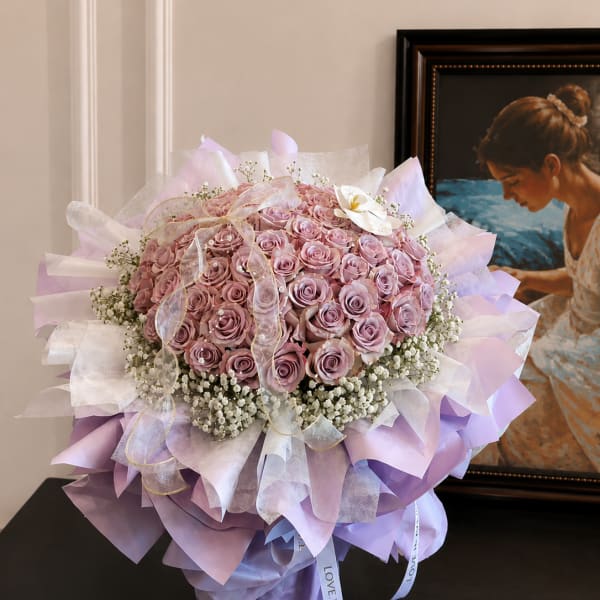 Large bouquet of pink roses wrapped in lavender paper with a ribbon