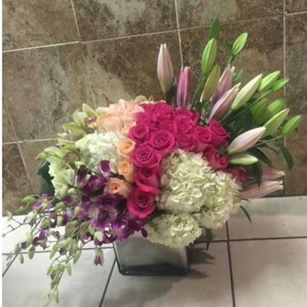 Mixed bouquet with pink roses, lilies, and white hydrangeas in a square vase