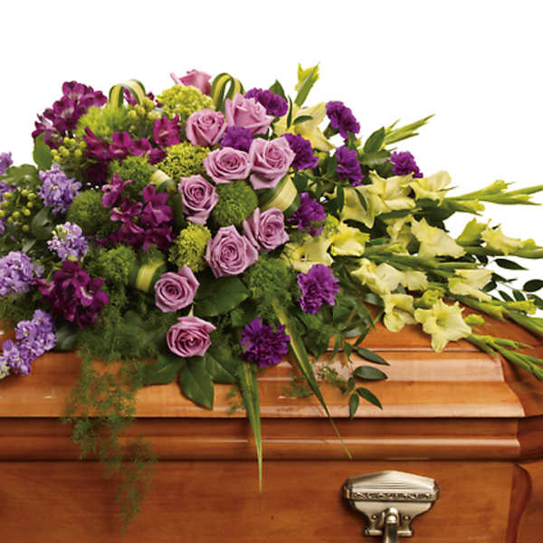 Purple, pink, and yellow flowers arranged on a wooden casket