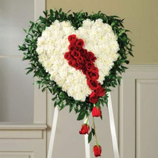 Heart-shaped floral wreath with white flowers and red roses on a stand