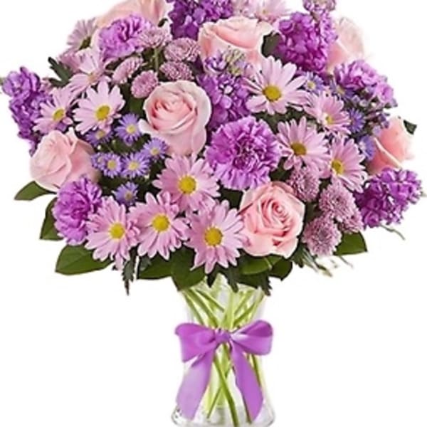 Pink and purple bouquet of roses and daisies in a glass vase with a ribbon