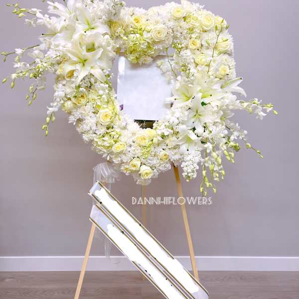White floral wreath on a stand with lilies and roses