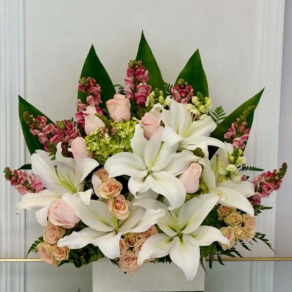 White lilies and pale roses arranged in a box with pink accents