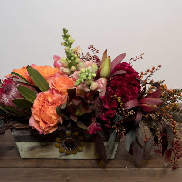 Low floral centerpiece with peach, burgundy, and green blooms in a rectangular container