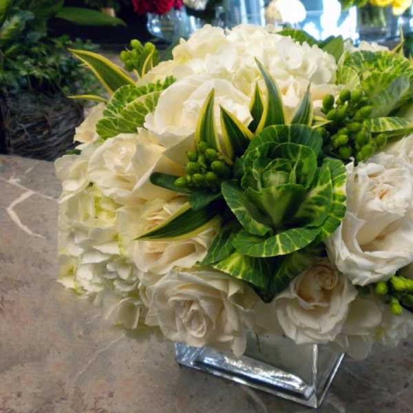 White rose bouquet with green variegated foliage in a square vase