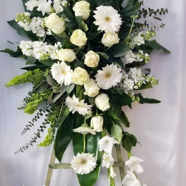Tall white floral standing spray on an easel with gerberas, roses, and gladiolus