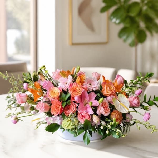 Low floral arrangement of pink, peach, and orange blooms in a white bowl vase