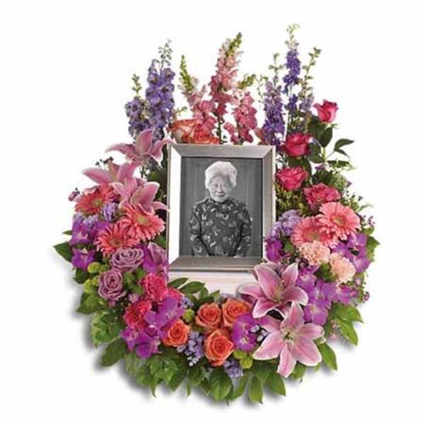 Sympathy wreath of mixed pink, purple, and orange flowers around a framed photo