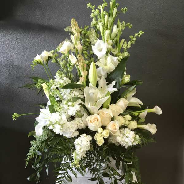Tall white floral arrangement with lilies and roses in a white container