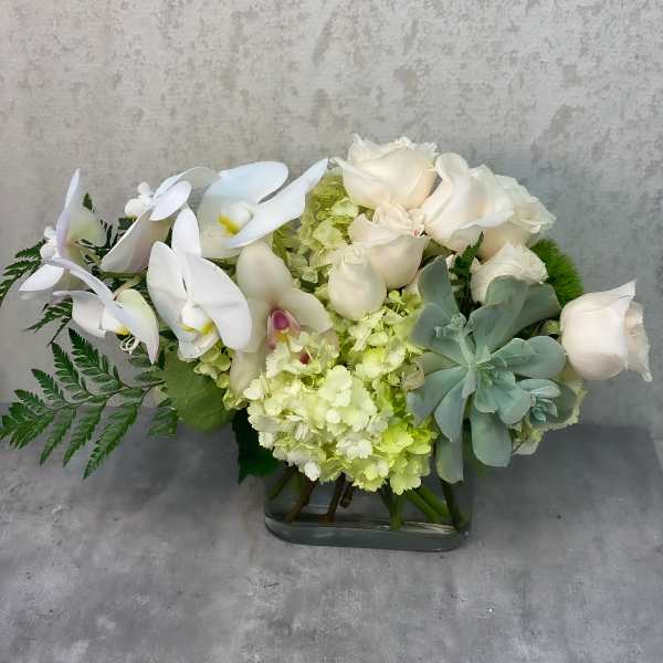 White orchids and roses arranged in a glass vase with pale green hydrangea
