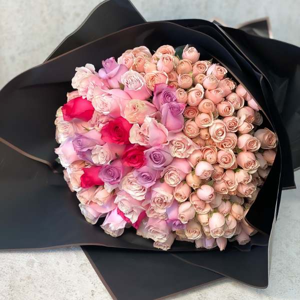Large bouquet of pink and lavender roses wrapped in black paper
