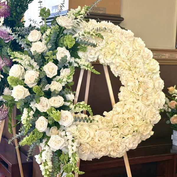 Large floral wreath of white roses and green accents on an easel.