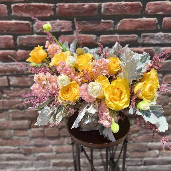 Yellow and pink floral arrangement in a dark vase on a stand