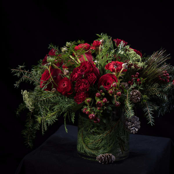 Red roses and winter greenery in a glass vase with pinecones and berries