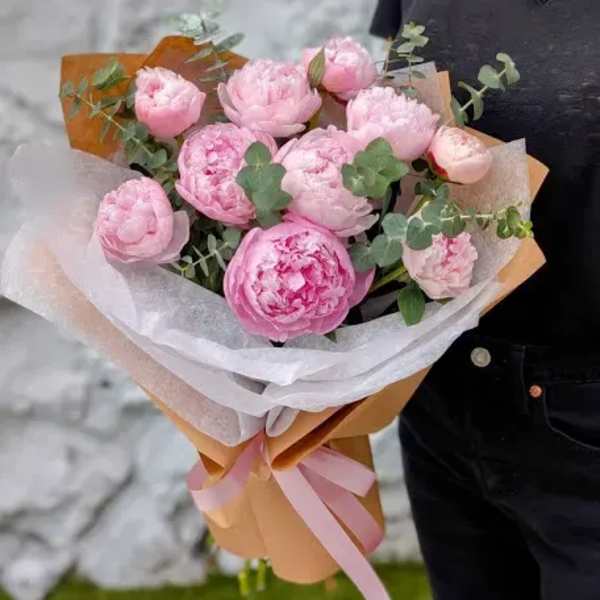 Bouquet of pink peonies wrapped in white and tan paper with a pink ribbon