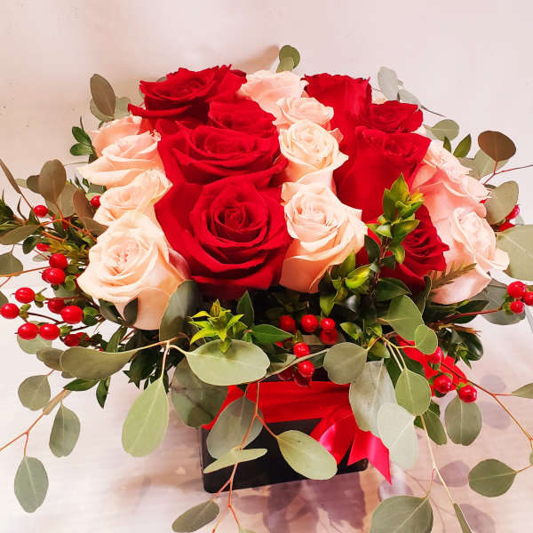 Red and blush roses arranged in a black box with eucalyptus and red berries