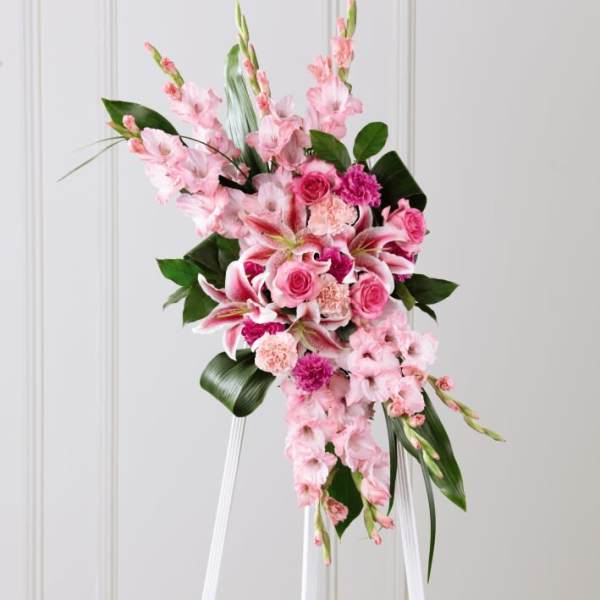 Tall pink standing floral spray on a white easel with roses, lilies, and carnations.