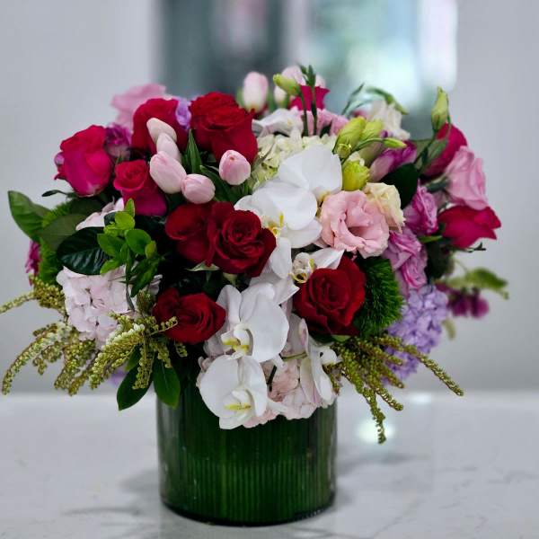 Mixed bouquet of red, pink, and white flowers in a green glass vase