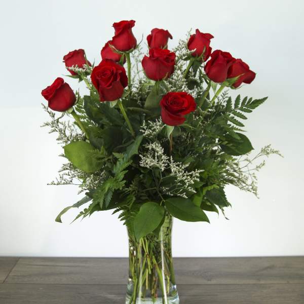 Red roses arranged in a clear glass vase with greenery