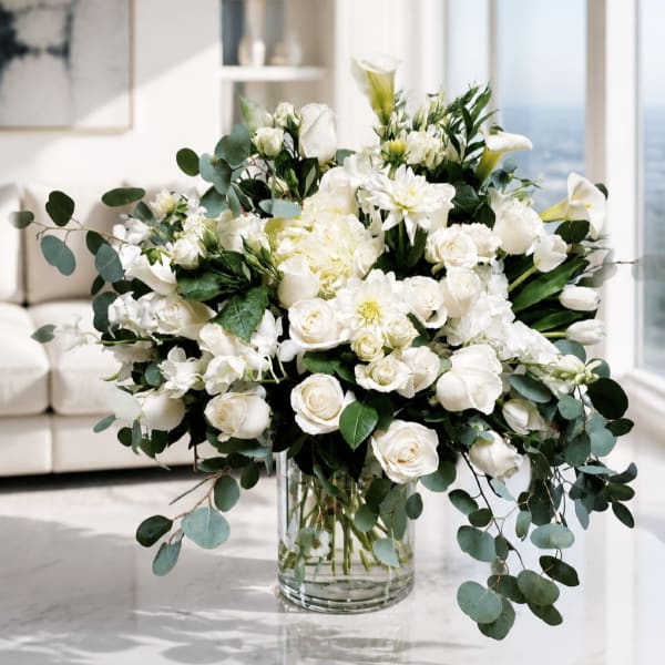 White floral arrangement in a clear glass vase with trailing eucalyptus