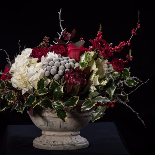 Red and white floral arrangement in a stone urn with berries and branches
