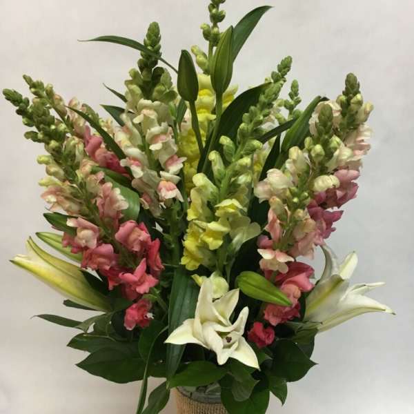 Tall bouquet of pink, yellow, and white snapdragons with white lilies in a burlap-wrapped vase