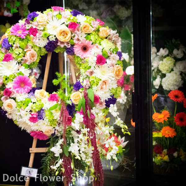 Large floral wreath on an easel with pink, white, peach, and purple flowers.