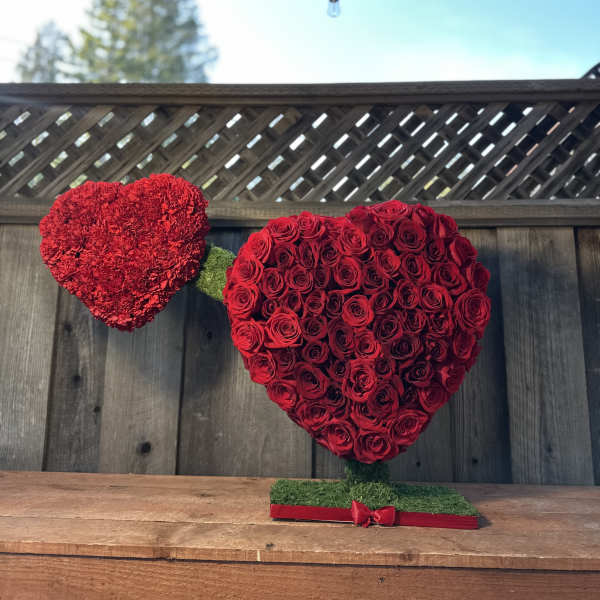 Two red heart-shaped floral arrangements on stands, one made of roses