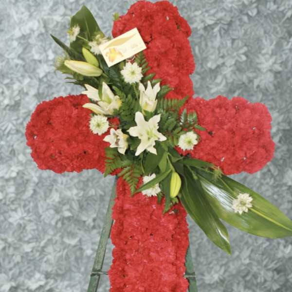 Red floral cross on a stand with white lilies and greenery